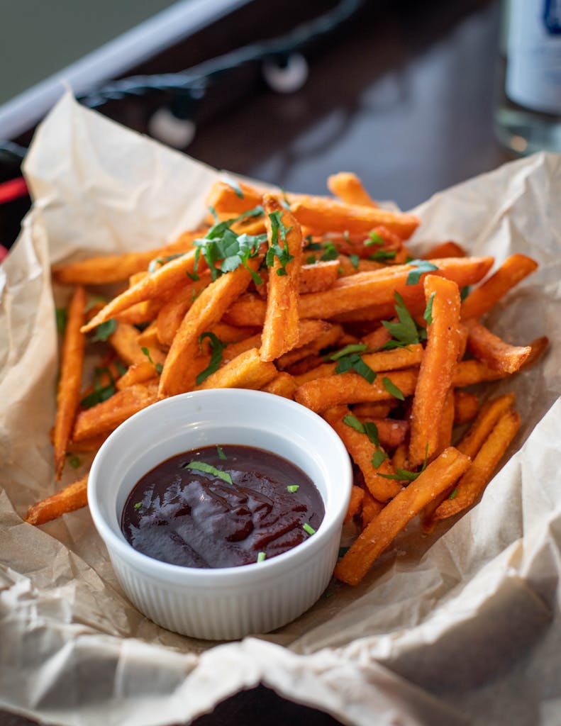 Appetizing sweet potato fries served with a rich dipping sauce, garnished with fresh herbs.